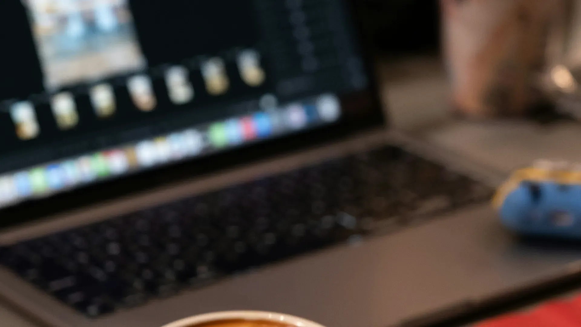 A laptop open on a desk next to a cup of coffee, with the screen softly out of focus