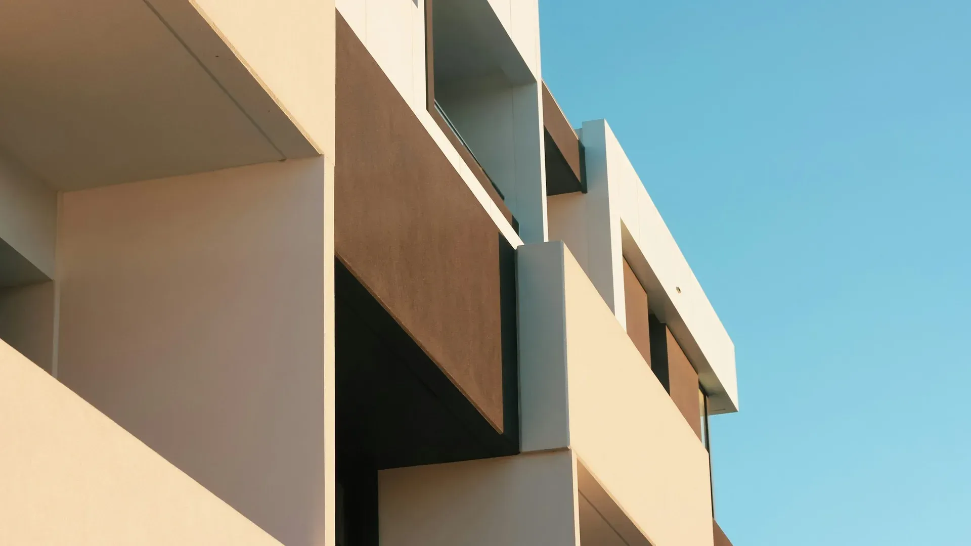Low-angle view of a modern apartment building's angular facade against a clear blue sky