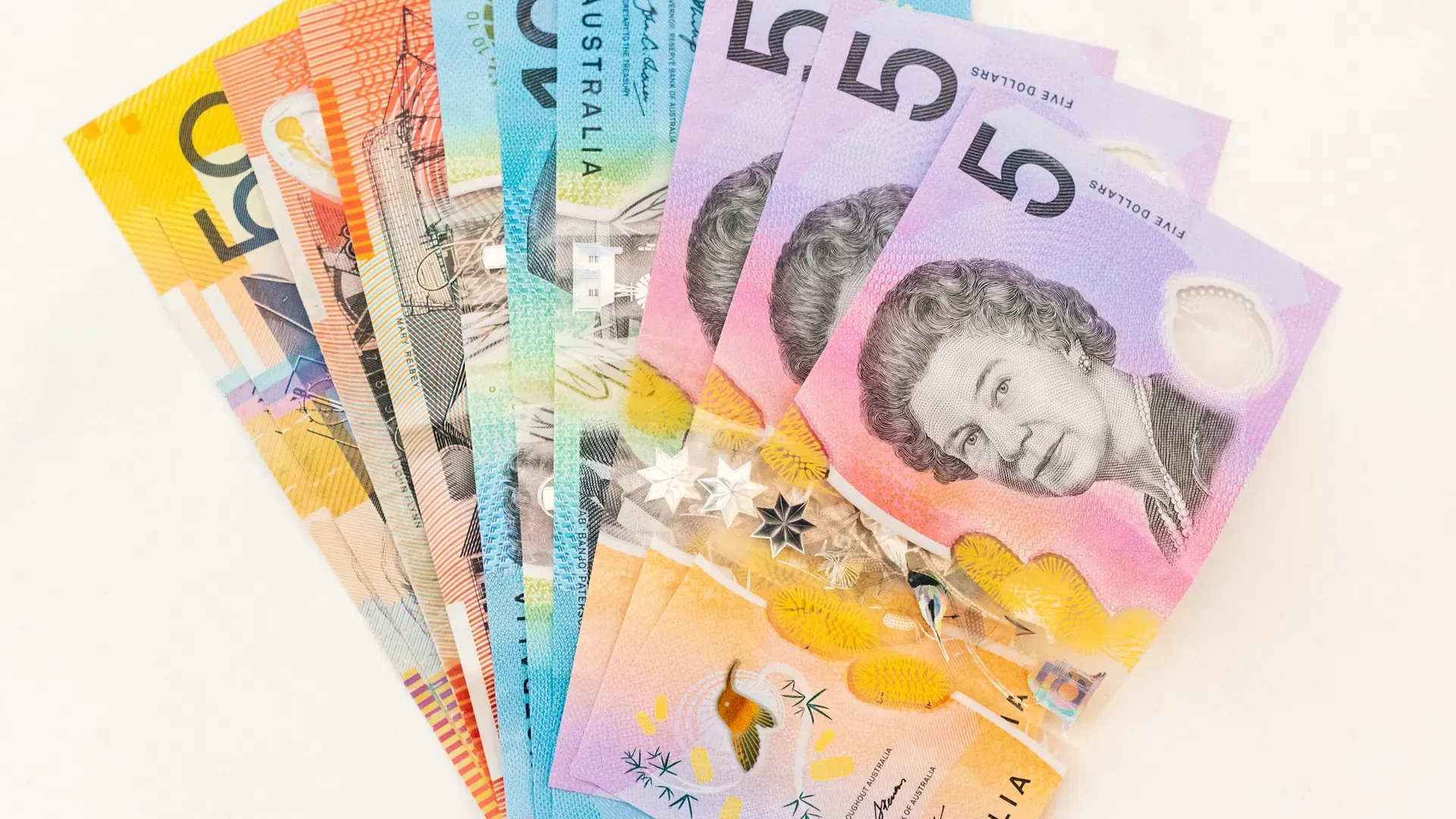 A fan of Australian banknotes in different colours laid out on a white surface