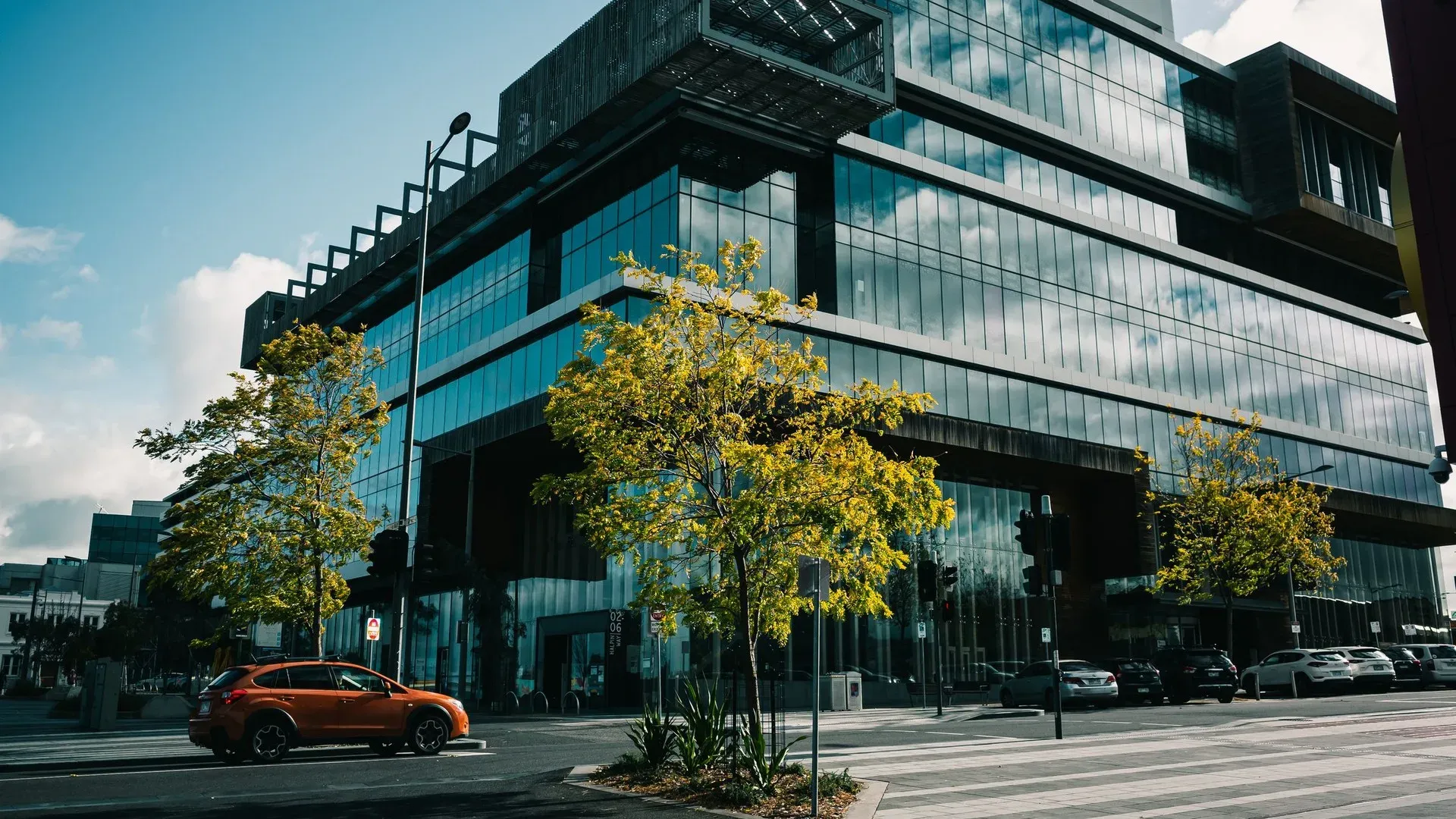 Exterior of a modern glass office building on an Australian street corner with trees and parked cars