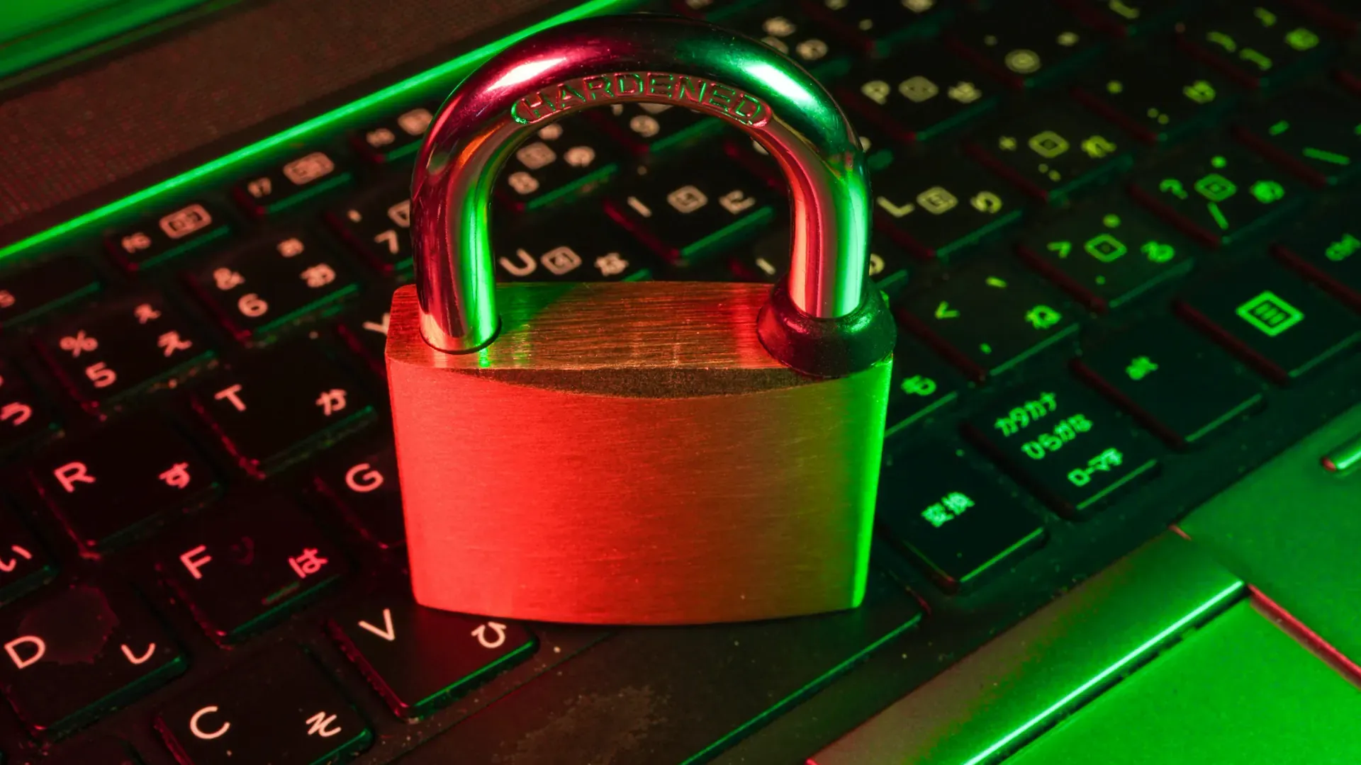 A red padlock resting on a black laptop keyboard lit with green and red light