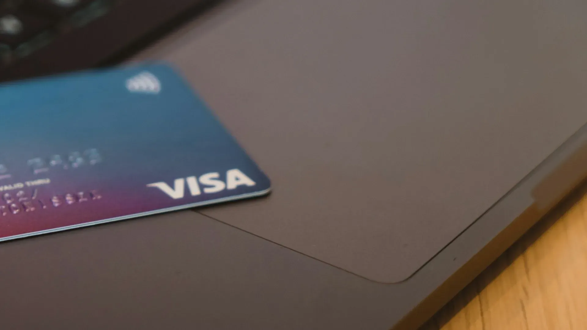 Close-up of a bank card with a Visa logo resting on a dark laptop keyboard, no faces in frame