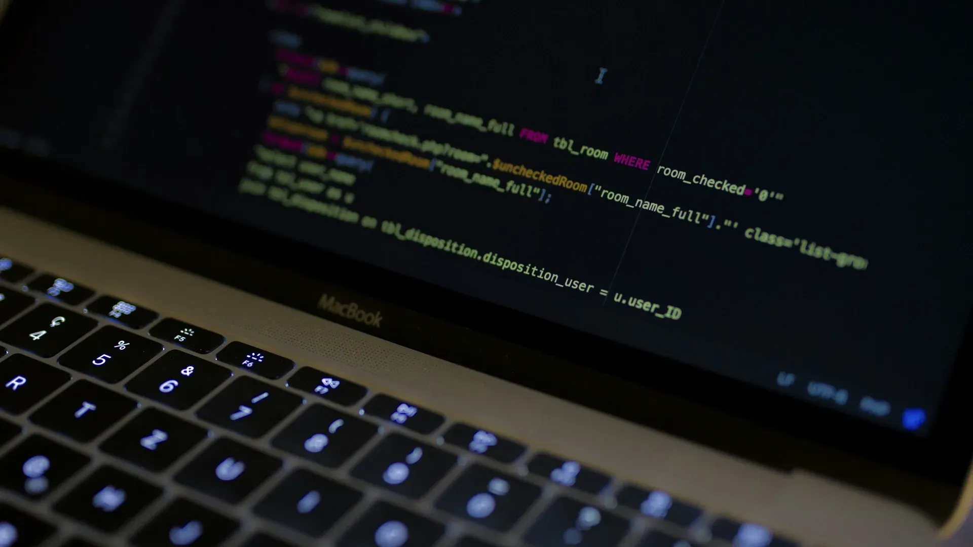 Close-up of a MacBook keyboard with syntax-highlighted code visible on the screen behind it