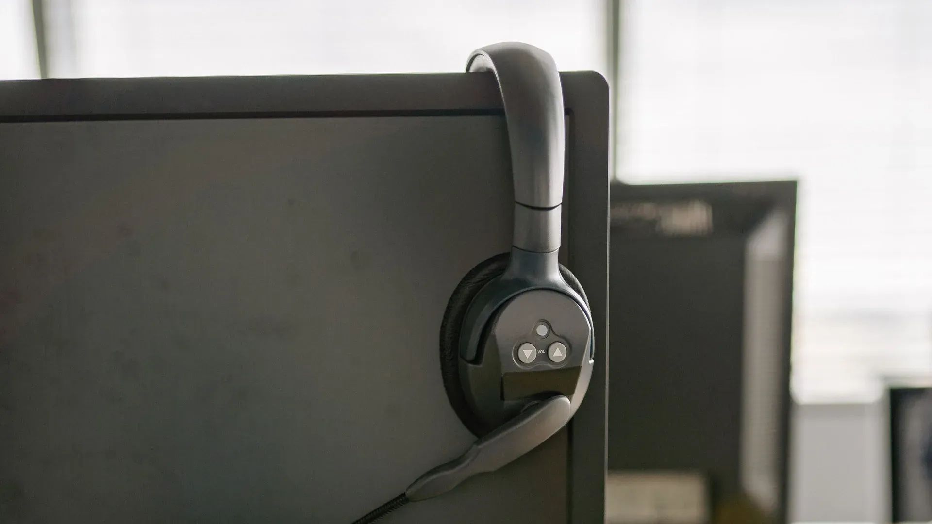 A telephone headset hanging on the edge of a computer monitor at an office desk